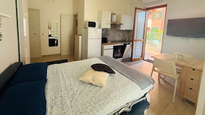 A compact room with a bed, a desk, a kitchenette, and a sliding door to an outdoor area. - Terrazza vicino alla spiaggia in centro (Marina di Andora)