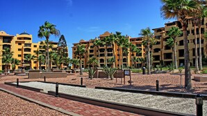A hotel courtyard with palm trees, a paved walkway, and a pool area. - PrincesaB108 GroundFlr Grill ExperienceRockyPoint Oversized Patio (Puerto Penasco)