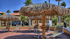 Outdoor lounge chairs under thatched umbrellas, a brick-paved area, and palm trees. - PrincesaB108 GroundFlr Grill ExperienceRockyPoint Oversized Patio (Puerto Penasco)
