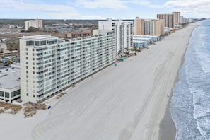 A beachfront hotel with multiple floors, a sandy beach, and a view of the ocean. - Seashells & Sand Traps
Oceanfront 2BR Condo - Stunning Views & Steps to Beach (Myrtle Beach)