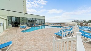 Uma área de piscina com cadeiras de descanso azuis e um edifício com a inscrição 'Sanda Beach Club'.