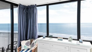 Varanda com vista para o oceano, penteadeira branca com objetos decorativos e cadeira com almofada listrada.