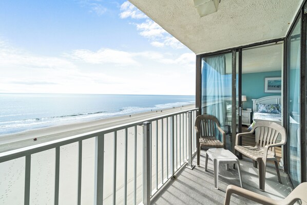 Een balkon met uitzicht op het strand, een glazen deur en twee stoelen.