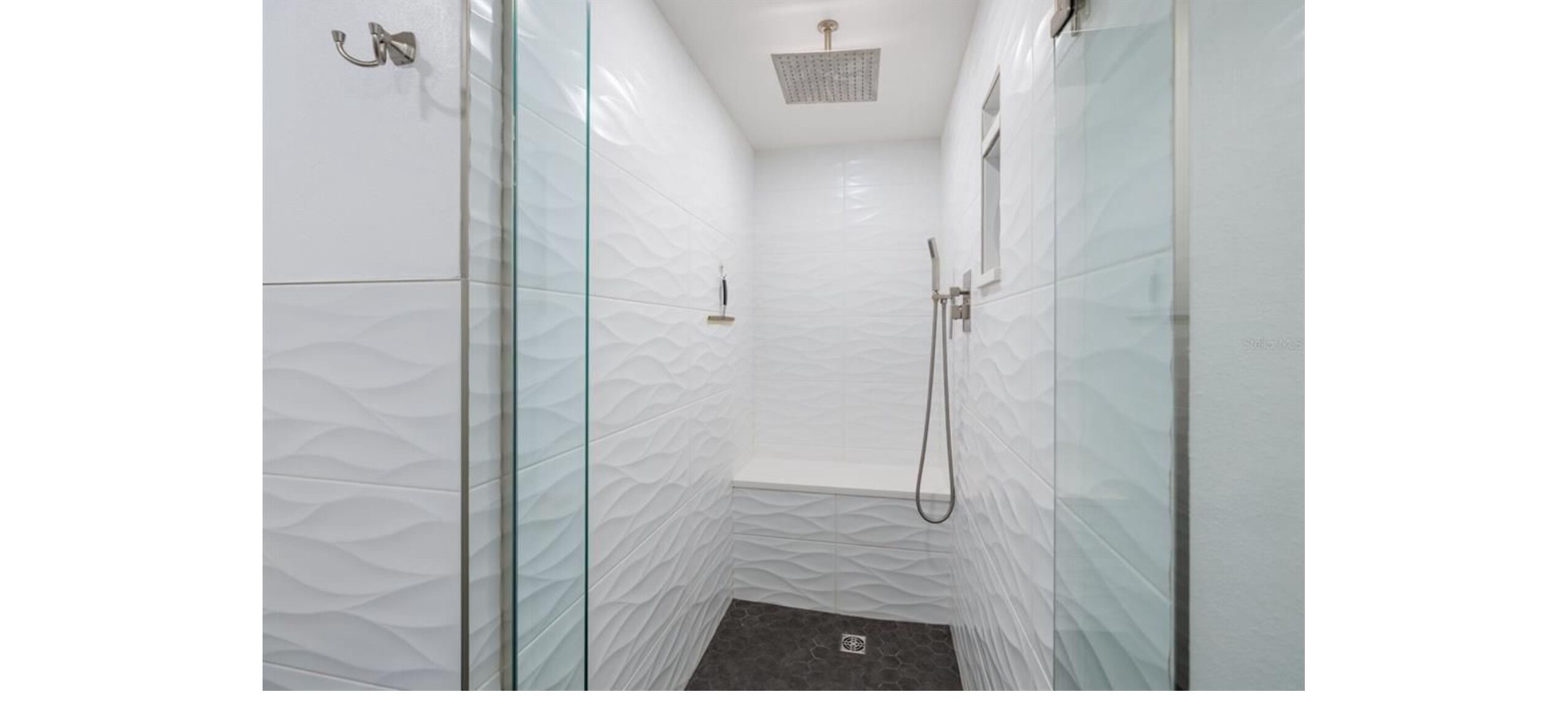 Een moderne badkamer met glazen douchedeuren, een douchekop en een handdouche.