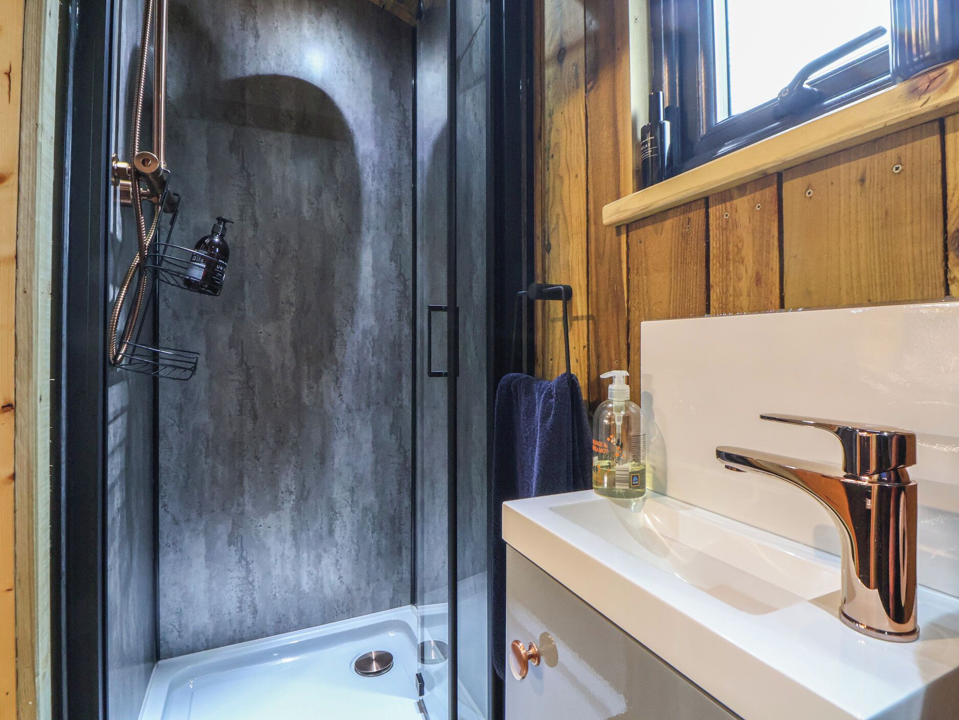 Un baño moderno con cabina de ducha de vidrio, un lavabo blanco con grifo cromado y paneles de madera.