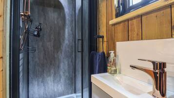 Un baño moderno con cabina de ducha de vidrio, un lavabo blanco con grifo cromado y paneles de madera.