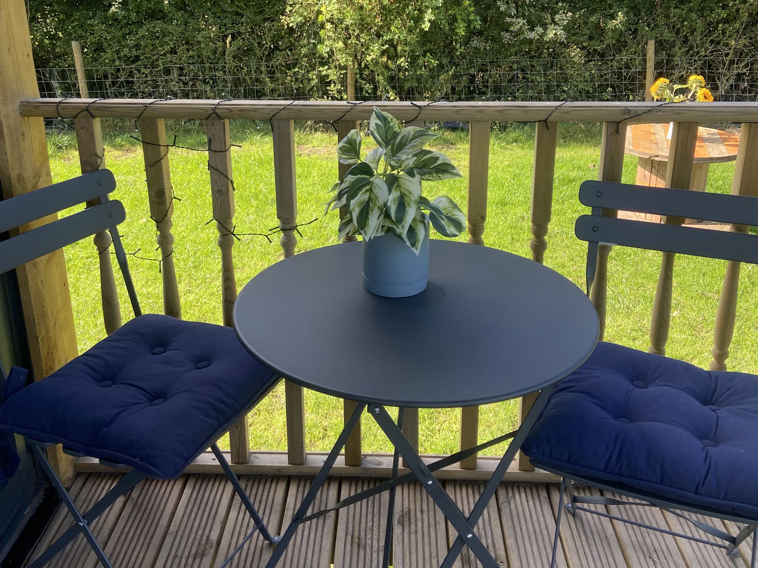 A wooden deck with a round table and two blue cushioned chairs.