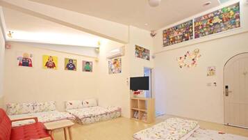 A child-friendly room with a sofa, a TV, and wall decorations including posters and a shelf with toys.