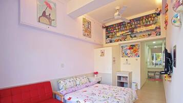 A bedroom with a bed, a red chair, a ceiling fan, and a wall with various decorations.