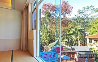 A traditional Japanese-style room with tatami flooring, a shoji screen, and a view of a traditional garden with a thatched-roof structure.