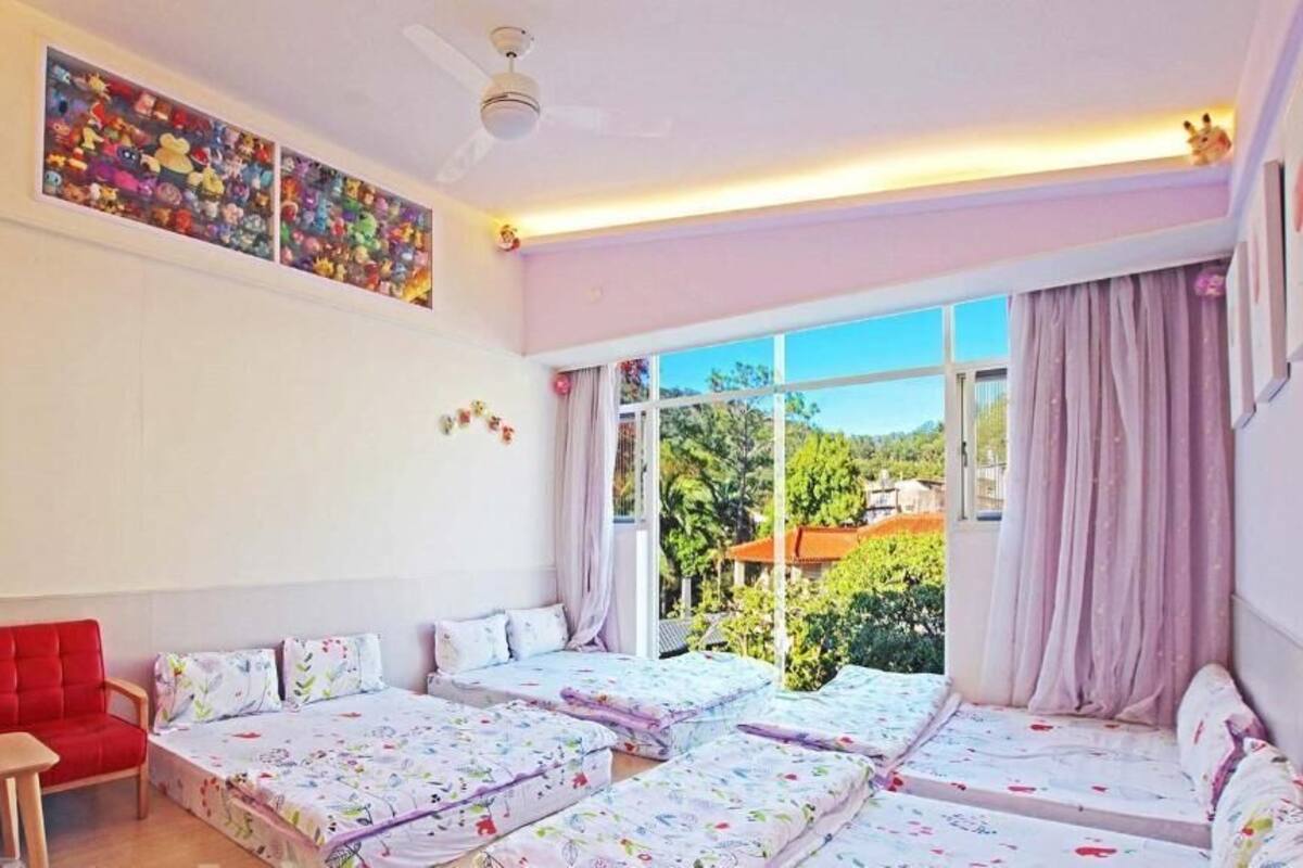 A room with a red sofa, two single beds, a small table, and a large window with curtains.