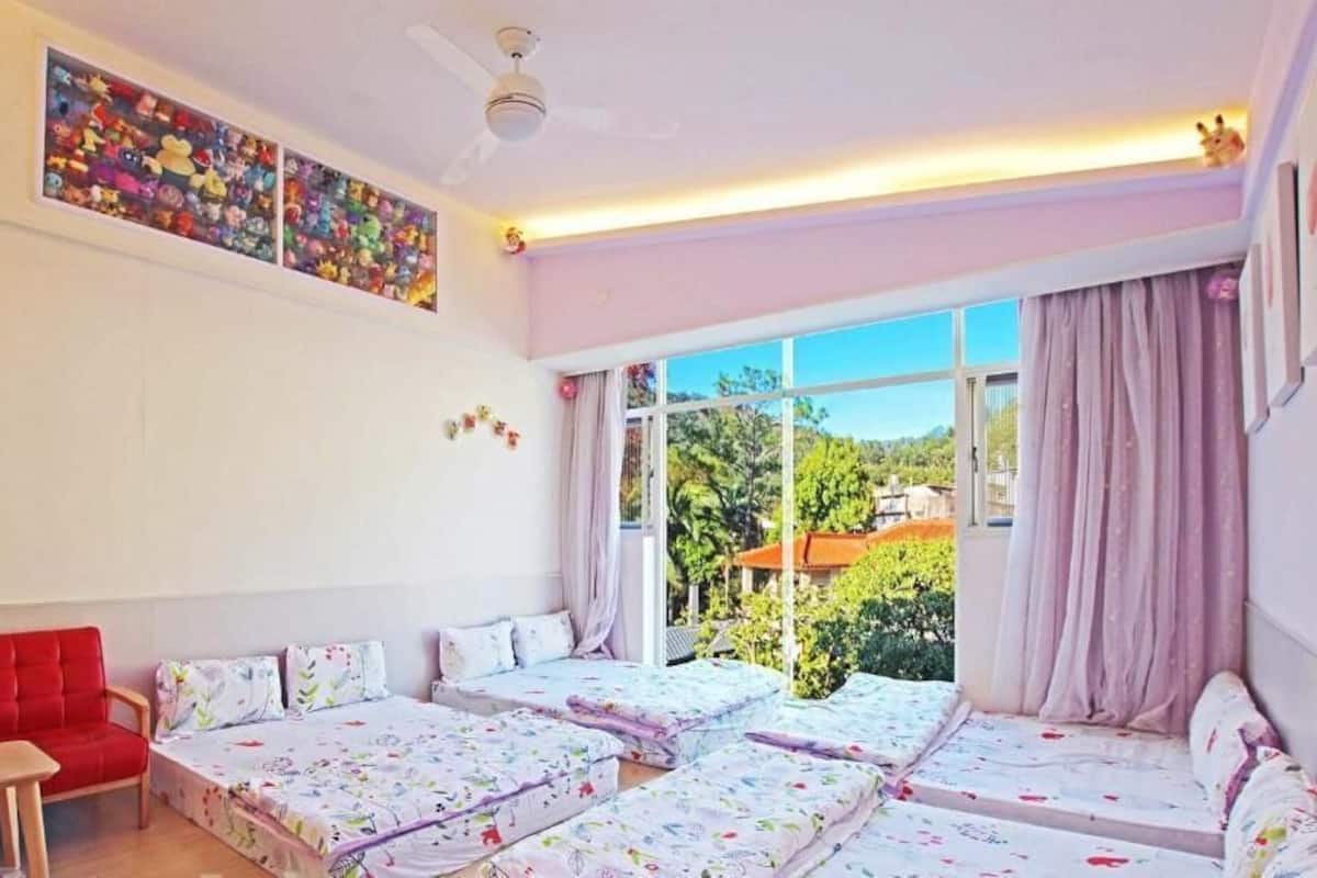 Una habitación con un sofá rojo, dos camas individuales, una mesita pequeña y un ventanal con cortinas.