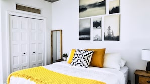 A bedroom with a bed, a bedside table, a mirror, and a wall with framed pictures. - Le1006 - Condo moderne (Québec)