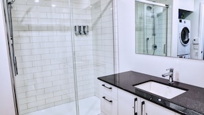 A modern bathroom with a glass-enclosed shower, a white sink with a black countertop, and a mirror above the sink. - Le1006 - Condo moderne (Québec)