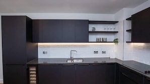 A modern kitchen with dark cabinetry, a central island, and a built-in sink. - 2 Bed Flat - Sleeps 6 - Parking - Wifi (London)