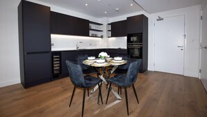 A modern kitchen with dark cabinetry, a central island with seating, and built-in appliances. - 2 Bed Flat - Sleeps 6 - Parking - Wifi (London)
