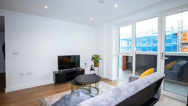 A modern living room with a flat-screen TV, a round table, and a sofa. - 2 Bed Flat - Sleeps 6 - Parking - Wifi (London)
