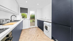 A compact kitchen with a built-in washing machine, a toaster, and a window overlooking greenery. - The Elphin Escape - 3 bedroom house (East Kilbride)