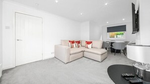 A modern living room with a beige sectional sofa, a dining area with a table and chairs, and a flat-screen TV mounted on the wall. - The Elphin Escape - 3 bedroom house (East Kilbride)