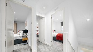 A modern hotel room with a large bed, a desk, and a wardrobe. There is a hallway leading to another room. - The Elphin Escape - 3 bedroom house (East Kilbride)