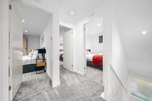 Ein modernes Hotelzimmer mit einem großen Bett, einem Schreibtisch und einem Kleiderschrank. Ein Flur führt zu einem weiteren Zimmer.