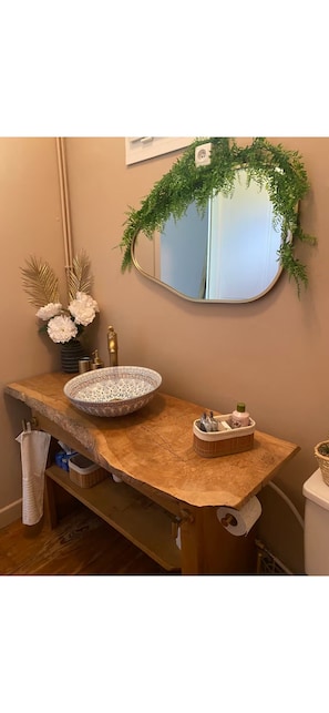A bathroom with a wooden vanity, a round mirror, a white vase with flowers, and a green plant decoration. - The blue house (Courniou)