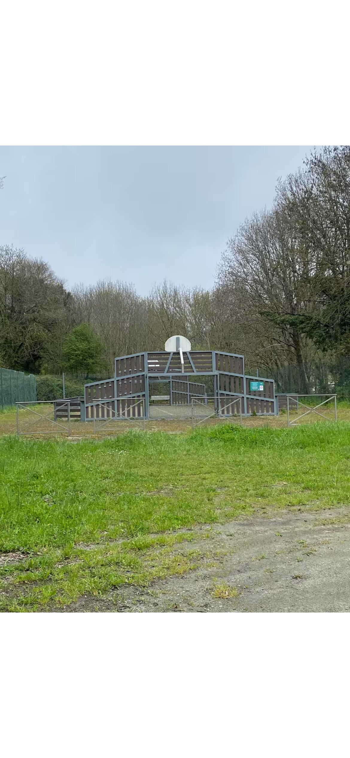 Un espace extérieur clos, doté d’une structure blanche, qui pourrait être un abri ou un local de stockage, et entouré d’arbres et d’herbe.