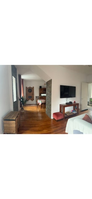 A spacious living area with a wooden floor, a television mounted on the wall, a dining table, and a cozy seating area with a couch. - The blue house (Courniou)