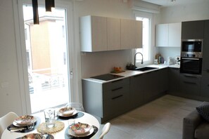 A modern kitchen with grey cabinets, a built-in oven, and a dining area with a round table set for four. - Claire SWeet Home L Apartment for groups or families near downtown and the ocean (Pesaro)