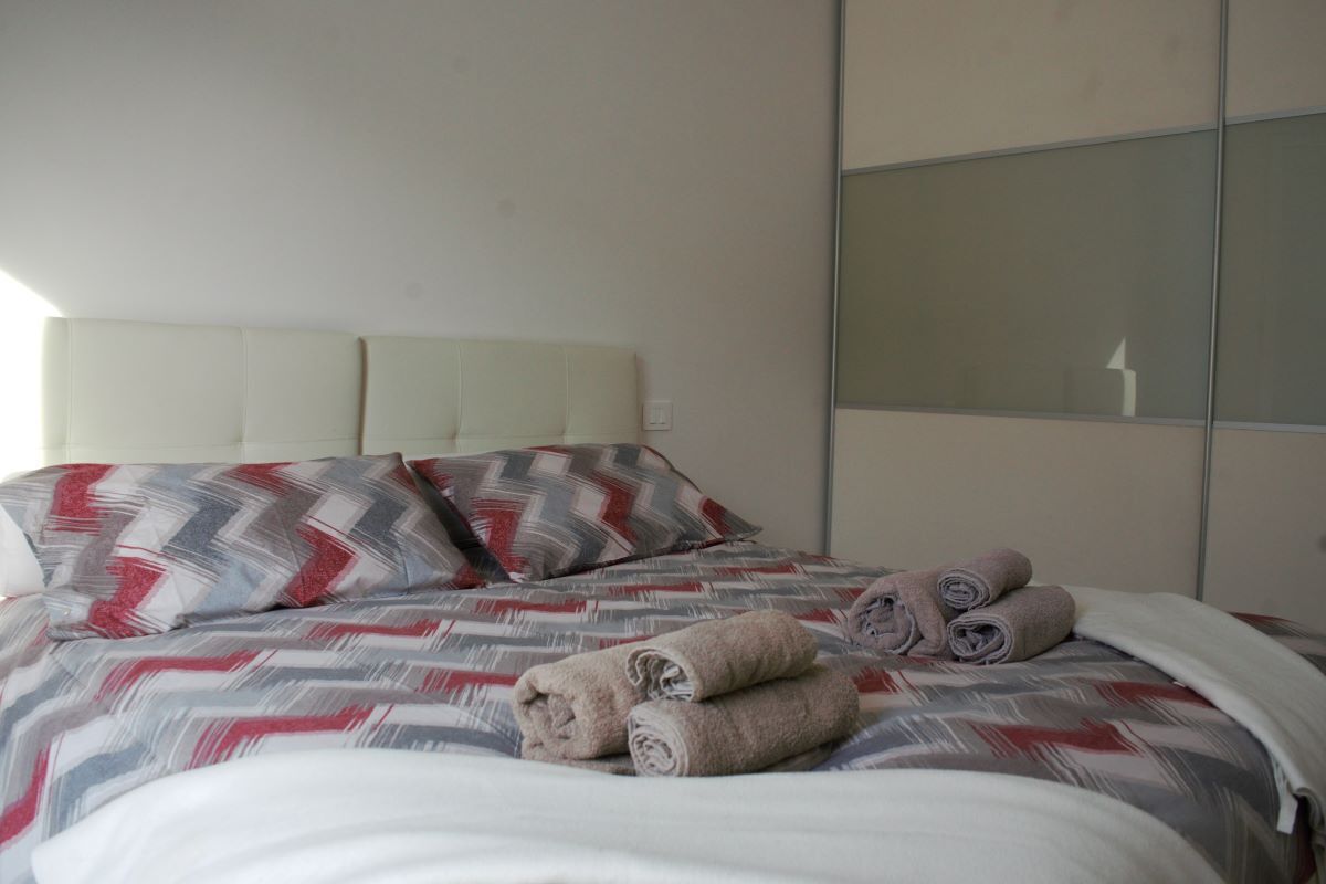 A neatly made bed with patterned bedding and rolled towels, a white headboard, and a large mirror on the wall.