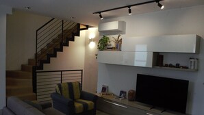 Un salon moderne comprenant un canapé, un fauteuil, un téléviseur à écran plat, un escalier et des étagères intégrées.