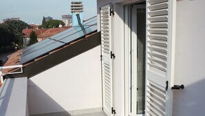 Un balcon doté d’un sol carrelé, de murs blancs et d’une porte avec des volets blancs.
