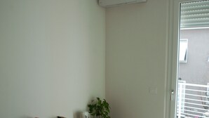 Une chambre d’hôtel avec un lit, une table de chevet avec des livres et un vase, une plante en pot et une fenêtre avec des stores.
