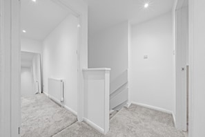 Un couloir aux murs blancs, avec un radiateur et un sol recouvert de moquette.