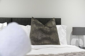 A neatly made bed with white linens and a single decorative pillow. - Loch Lomond Hillside Retreat (Alexandria)