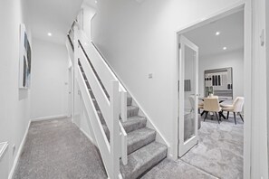 A modern interior with a staircase, a dining area with a table and chairs, and a wall with a geometric art piece. - Loch Lomond Hillside Retreat (Alexandria)