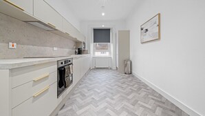 Una cocina moderna con piso de espiga, armarios blancos y un cubo de basura visible.