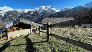 A mountain lodge with a wooden structure, a stone wall, and a view of snow-capped mountains. - Cozy Engadine house with a unique view! (Valchava)