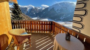 A balcony with a wicker chair and a small table, overlooking a snowy mountain range. - Cozy Engadine house with a unique view! (Valchava)