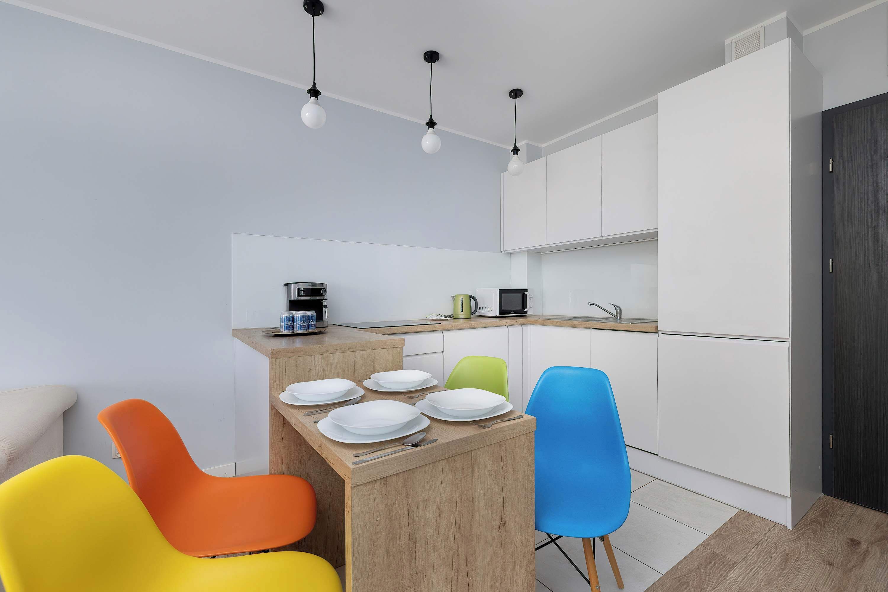 Una cocina moderna con armarios blancos, una isla de madera con platos y sillas coloridas.
