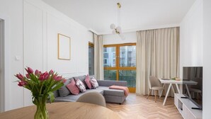 A modern living room with a sofa, dining table, and a TV. - Malila Apartments Cracow Rakowicka 254 (Kraków)