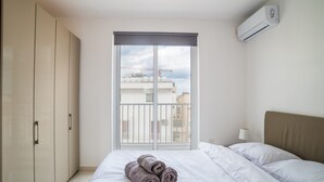 A hotel room with a bed, a wardrobe, a window with a view of buildings, and an air conditioning unit. - 2BR Penthouse with Private Terrace and Sea Views! (Saint Julian's)