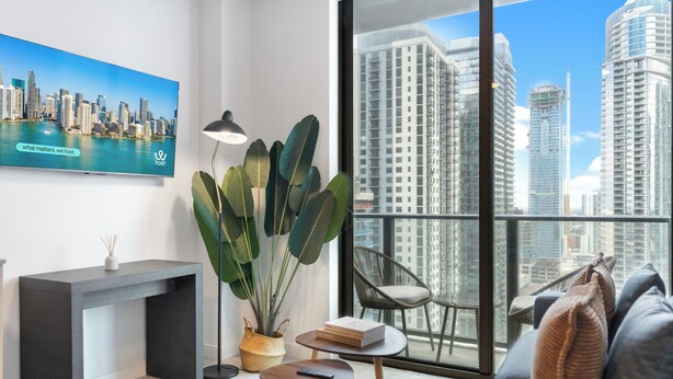 Una sala de estar moderna con vista a un paisaje urbano, una planta grande, un sofá, una mesita y una consola.