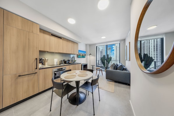 A modern kitchen with wooden cabinets, a dining table with chairs, and a large window with a city view. - Bayfront Park Building - Prime Miami Location - We Host (Miami)