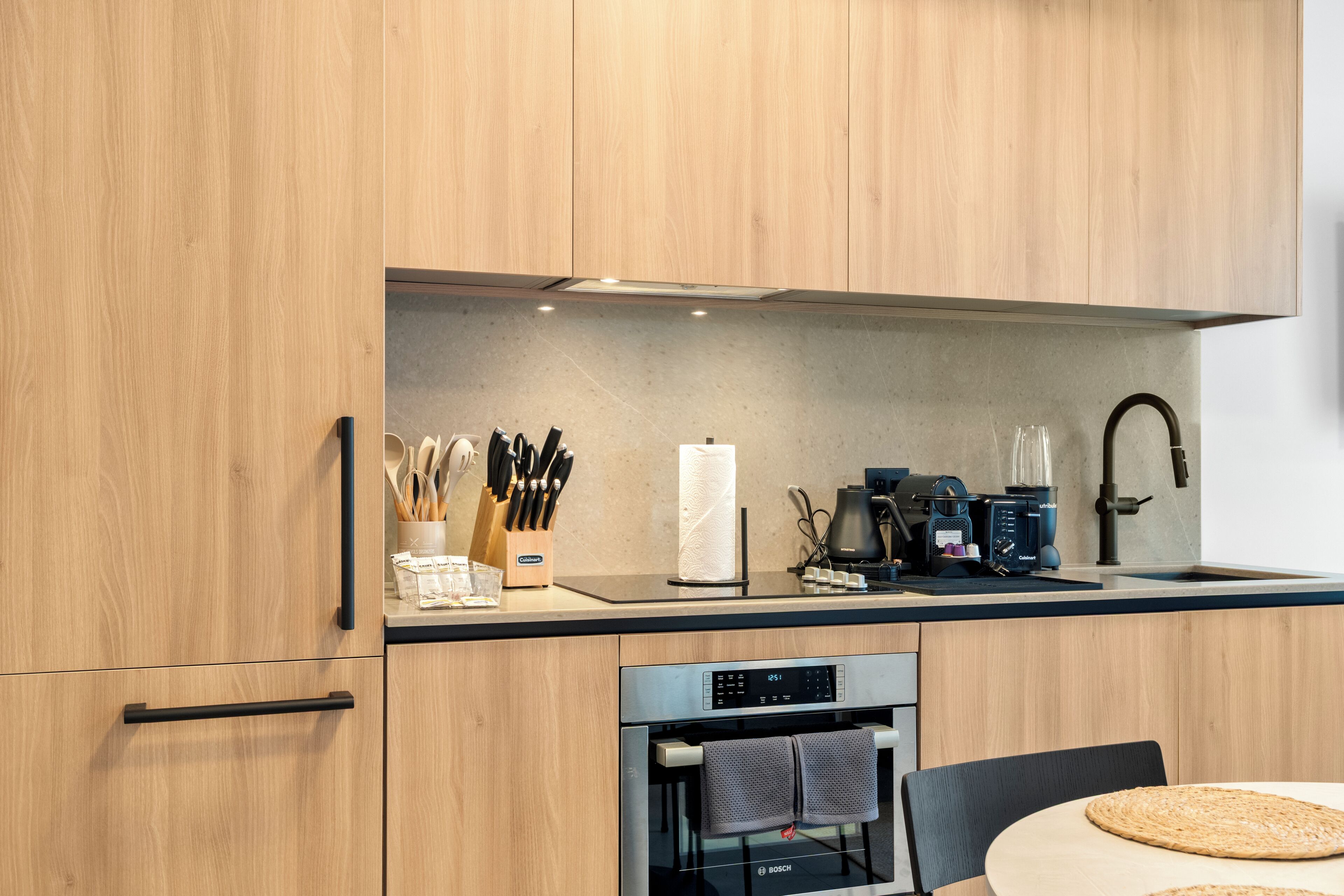 A modern kitchen with wooden cabinets, a Bosch oven, a coffee maker, and a sink.