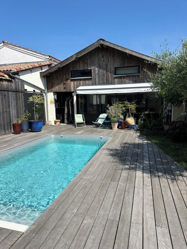 Une terrasse en bois avec une piscine, un patio couvert et des plantes en pot.
