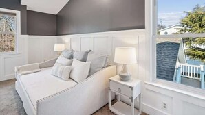 Een slaapkamer met een groot bed, twee nachtkastjes en een raam met uitzicht op een huis en bomen.