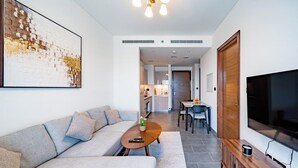 Ett modernt vardagsrum med en soffa, ett soffbord och en tv. Det finns också en matplats med ett bord och stolar, och ett kök syns i bakgrunden.