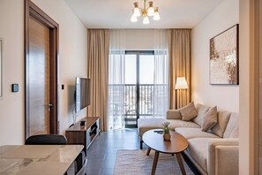 Ein modernes Wohnzimmer mit Sofa, Couchtisch, Fernseher und einem Balkon mit Vorhängen.