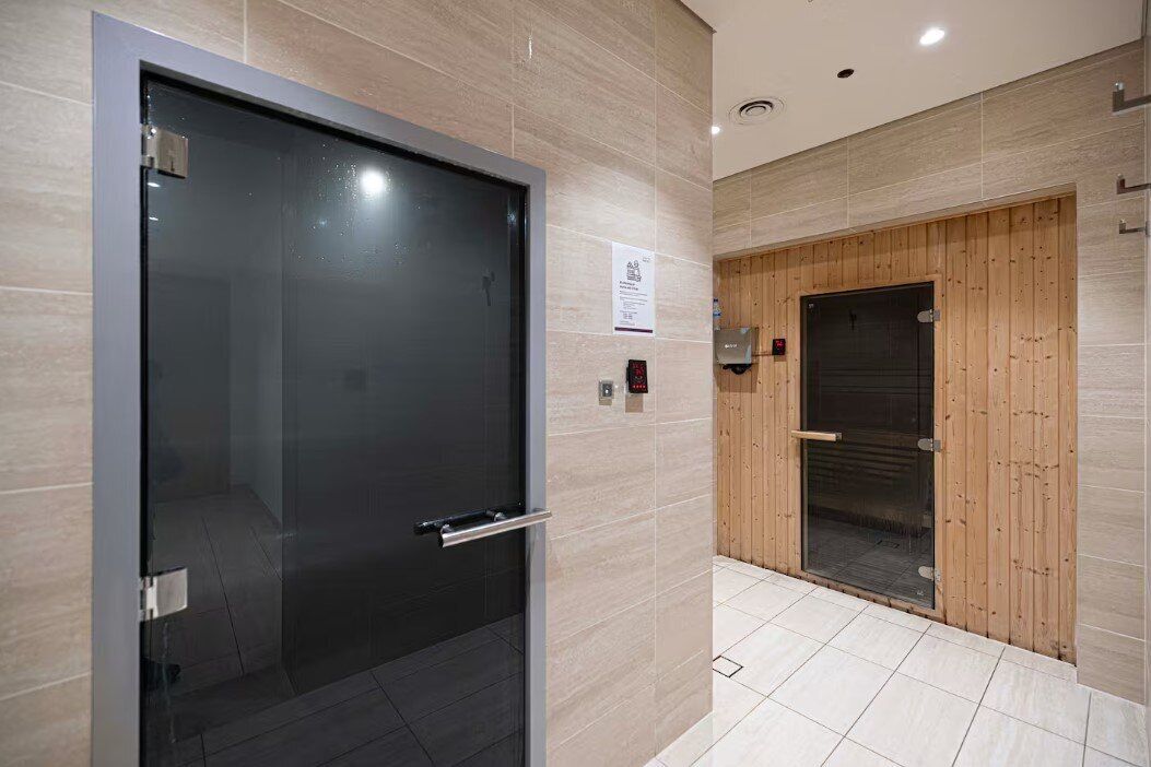 Een moderne lift met een metalen hendel en een glazen deur, naast een liftdeur met houten lambrisering.